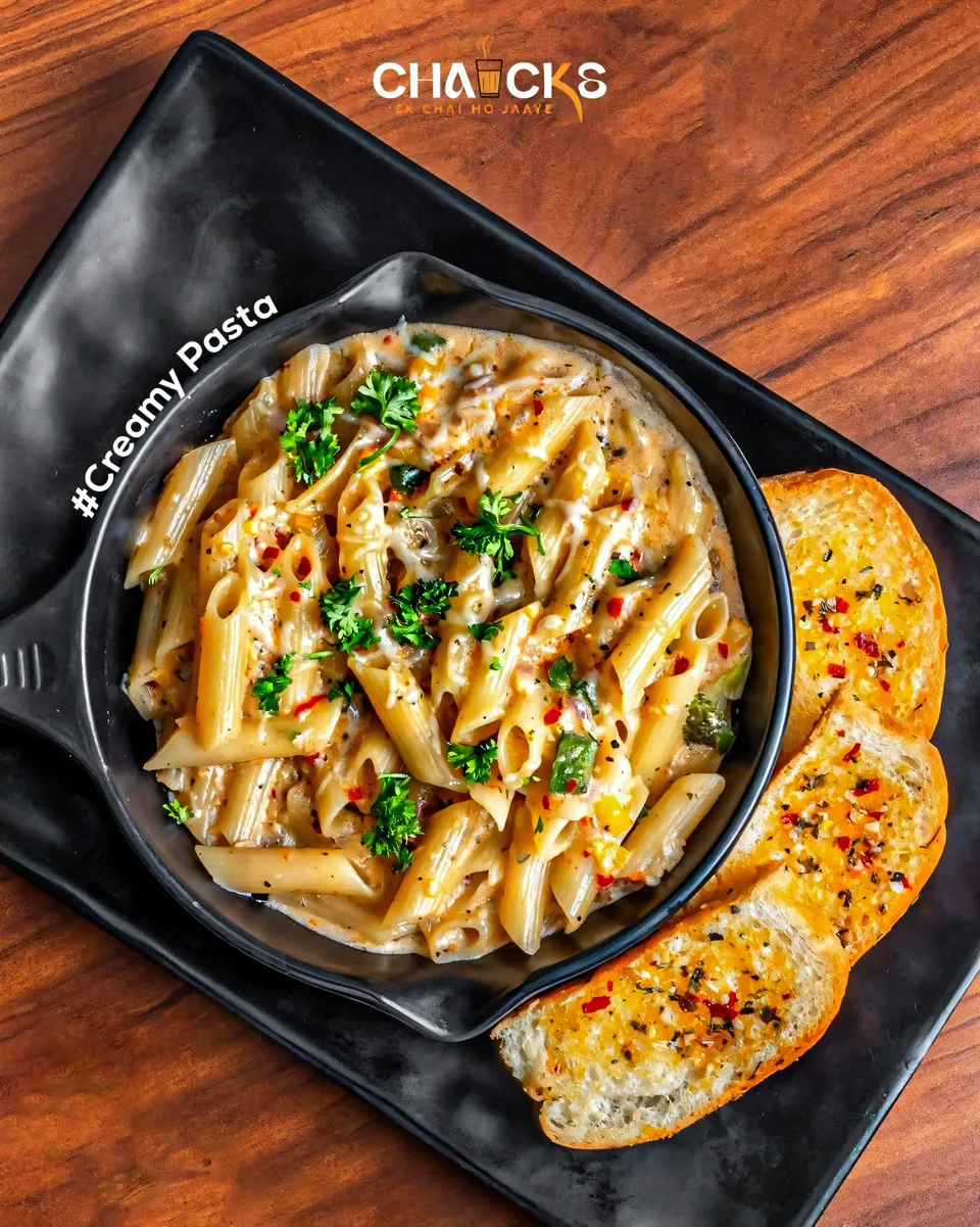Creamy penne pasta in a black skillet with garlic bread
