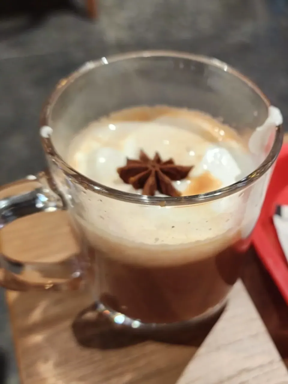 A glass mug of spiced hot chocolate topped with cream and a star anise